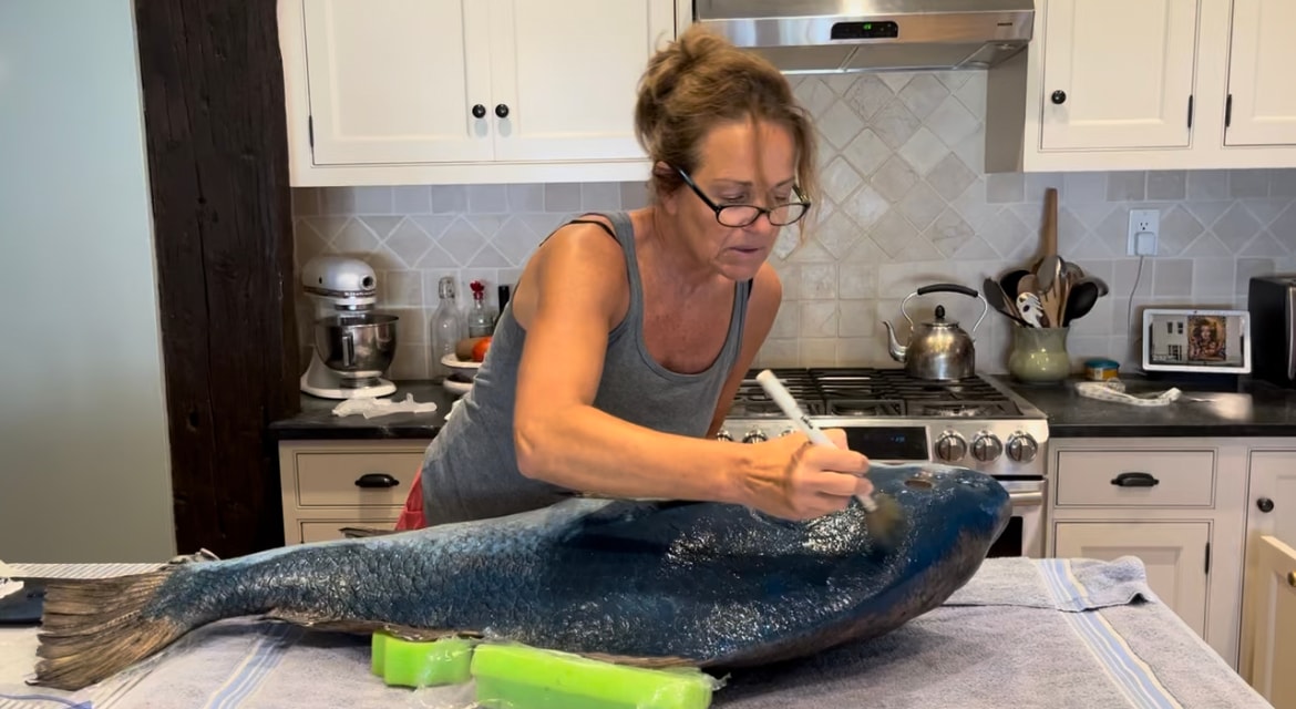Bridget inking a fish outdoors on a blue foam board